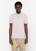 Junger Mann mit dunkler Haut, der ein hellrosa Poloshirt mit kurzen Ärmeln und beigefarbene Hosen trägt, vor einem schlichten weißen Hintergrund stehend.