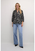 Schwarze Bluse mit floralen Mustern, lockerer Passform und Dreiviertelärmeln, kombiniert mit hellblauen weitem Beinkleid und spitzen schwarzen Schuhen.