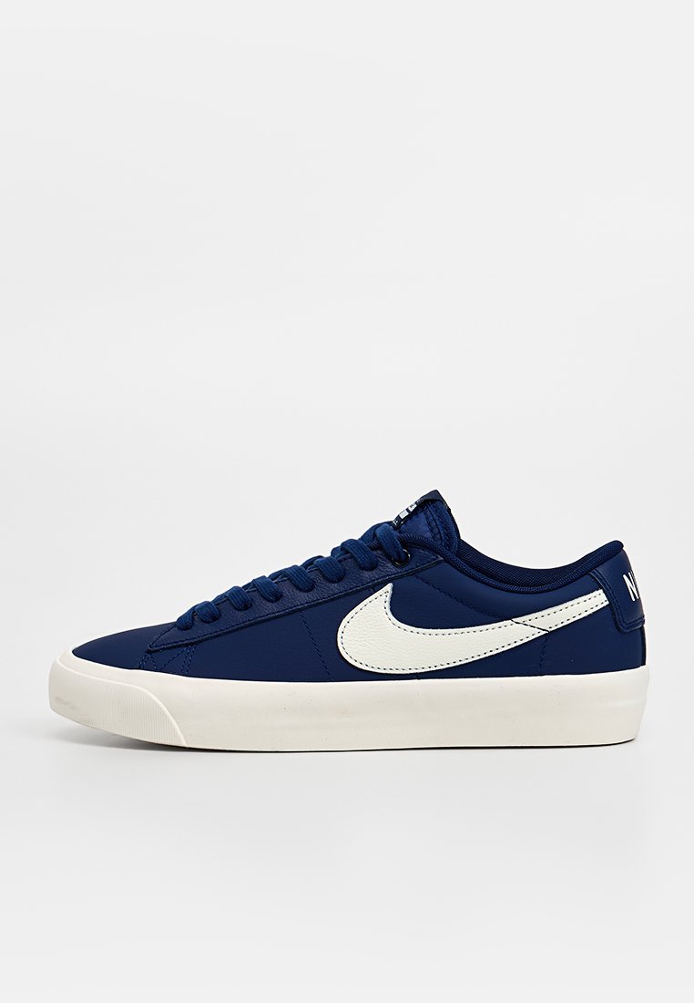 Marineblaue Sneaker mit flachem Design, weißem Swoosh-Logo und strukturiertem Stoffobermaterial. Verfügt über eine weiße Gummisohle und eine Schnürung.