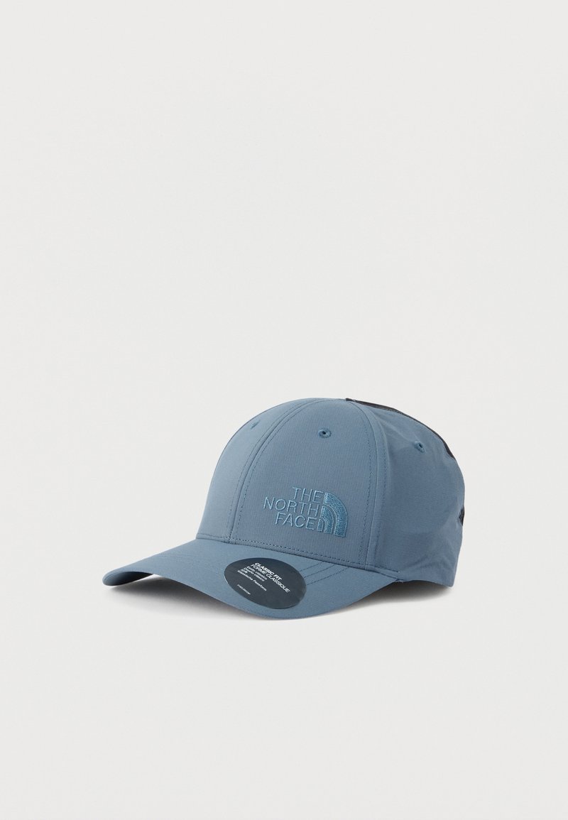 Blaues Cap mit gebogenem Schirm, vorne mit dem Sticklogo "The North Face" und einem schwarzen Aufkleber auf dem Schirm vor weißem Hintergrund.