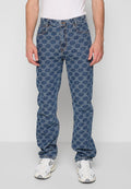 Mann trägt blue Jeans mit einem hellen geometrischen Kettenmuster, weiße Sneaker und ein weißes T-Shirt, steht vor einem schlichten Hintergrund.