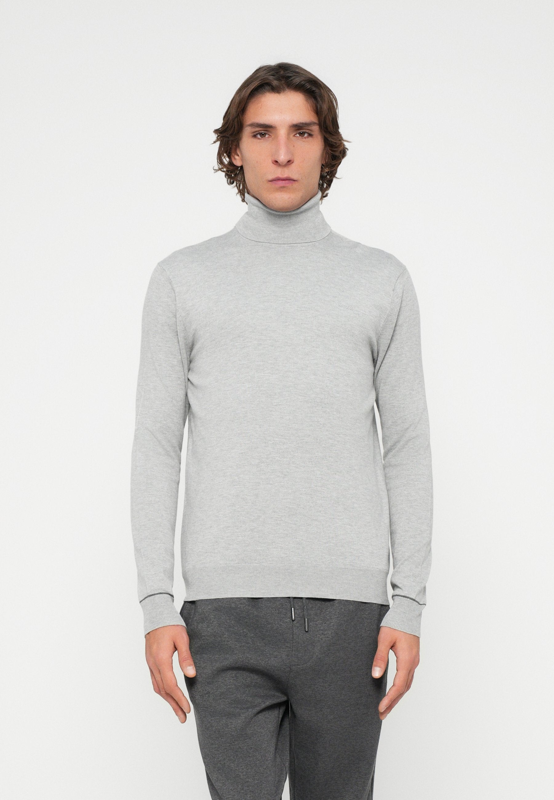 Hellgrauer Rollkragenpullover aus weichem, geripptem Material mit enganliegenden Ärmeln und Saum, getragen zu dunkelgrauen Hosen. Schlichtes Design ohne Muster.