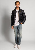 Schwarze gepolsterte Jacke mit hohem Kragen, Reißverschluss und gesteppter Textur, kombiniert mit einem weißen T-Shirt und hellblauen, ausgewaschenen Jeans.