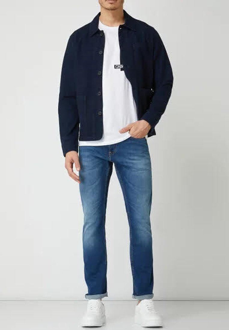 Marineblaues Hemd über einem weißen T-Shirt, kombiniert mit hellblauen Slim-Fit-Jeans und weißen Sneakers. Verfügt über ein lässiges, modernes Design.
