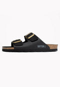 Schwarze Sandalen mit zwei verstellbaren Riemen und goldenen Schnallen, ausgestattet mit einem Korkfußbett und einer strukturierten schwarzen Außensohle. Bayton-Logo an der Seite.