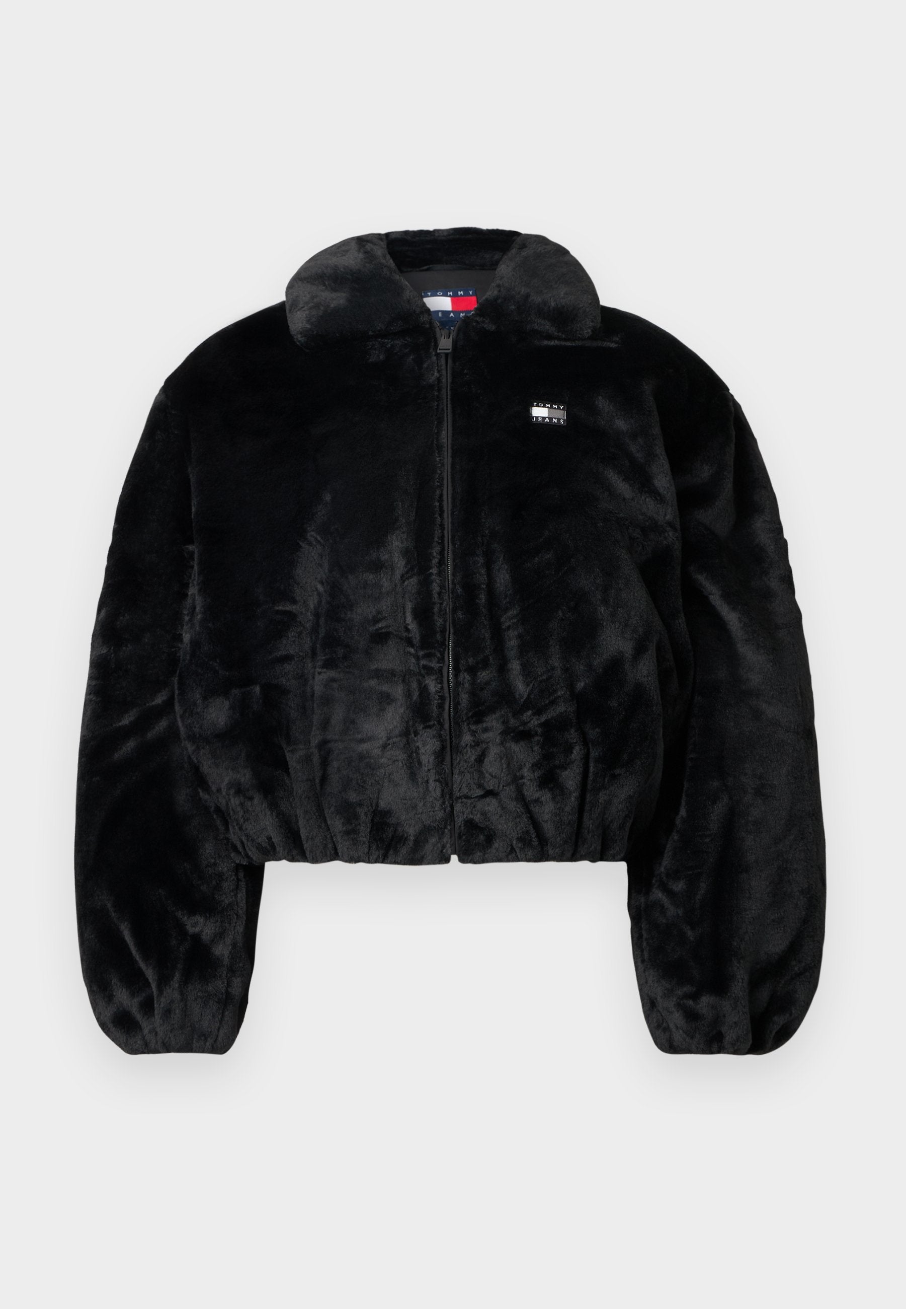 Schwarze kurze Jacke aus weichem Kunstpelz mit Reißverschluss, großem Kragen und elastischem Bund. Verfügt über ein kleines Logo-Patch auf der Brust.