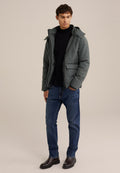 Geplüschte dunkelgrüne Jacke mit Kapuze, Fronttaschen, schwarzem Pullover, blauer Jeans und dunklen Stiefeln. Glatte Textur und lässiger Schnitt.