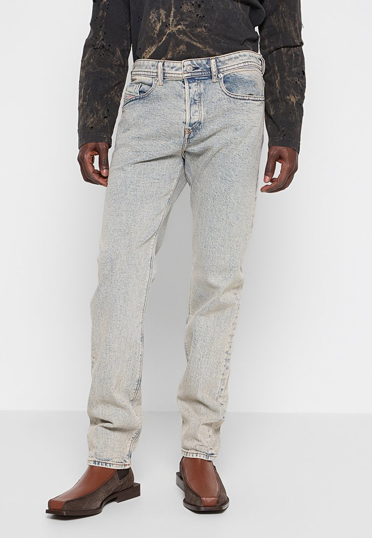 Ausgebleichte blaue Jeans mit geradem Bein und leichten Gebrauchsspuren, kombiniert mit braunen Slippern, die über texturierte Akzente und ein einzigartiges Design verfügen.
