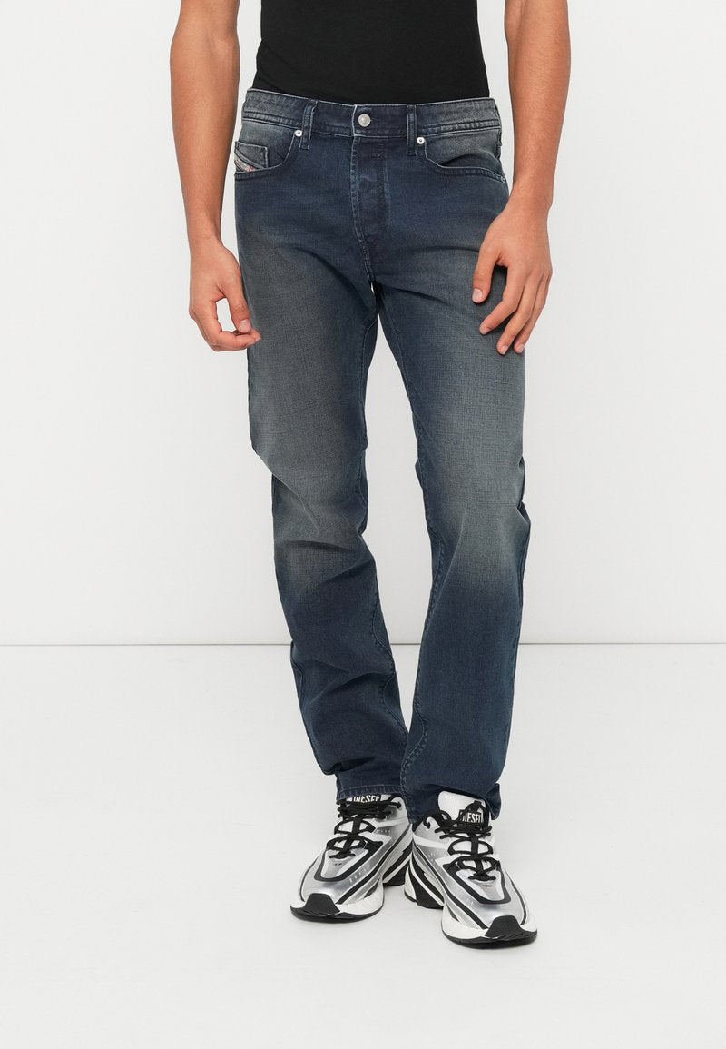 Dunkelblaue Jeans aus Denim mit leicht ausgewaschenem Finish, ausgestattet mit fünf Taschen, einem Knopfverschluss und einem gerade geschnittenen Bein. Dazu schwarze Sneakers getragen.