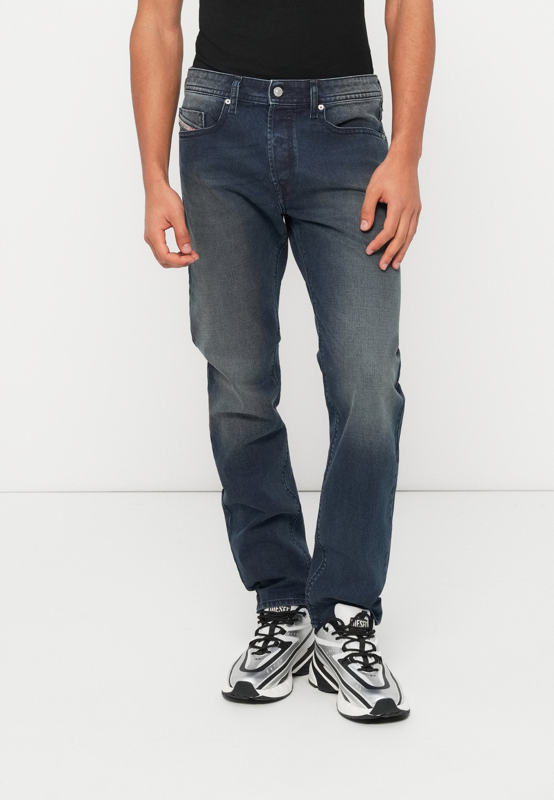 Dunkelblaue Jeans aus Denim mit leicht ausgewaschenem Finish, ausgestattet mit fünf Taschen, einem Knopfverschluss und einem gerade geschnittenen Bein. Dazu schwarze Sneakers getragen.