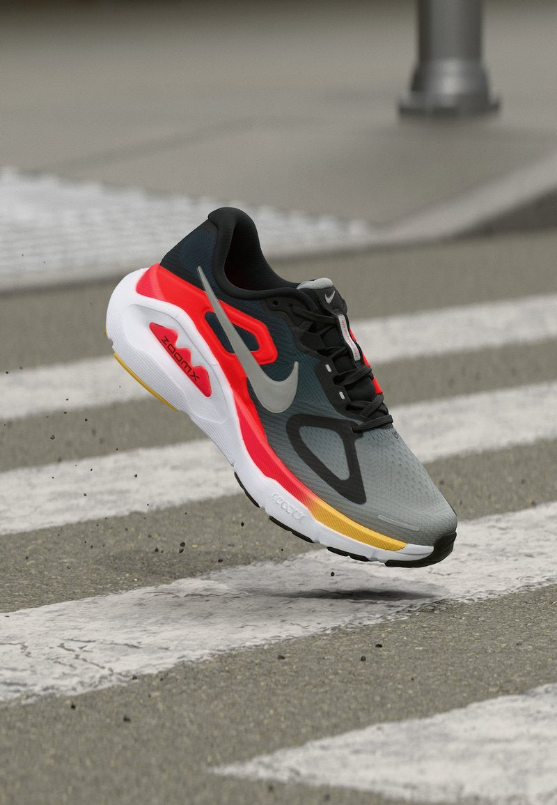 Grauer und schwarzer Nike-Laufschuh mit roten und gelben Akzenten, der über einem Zebrastreifen angehoben wird und die Sohle sowie die Seitenansicht zeigt.