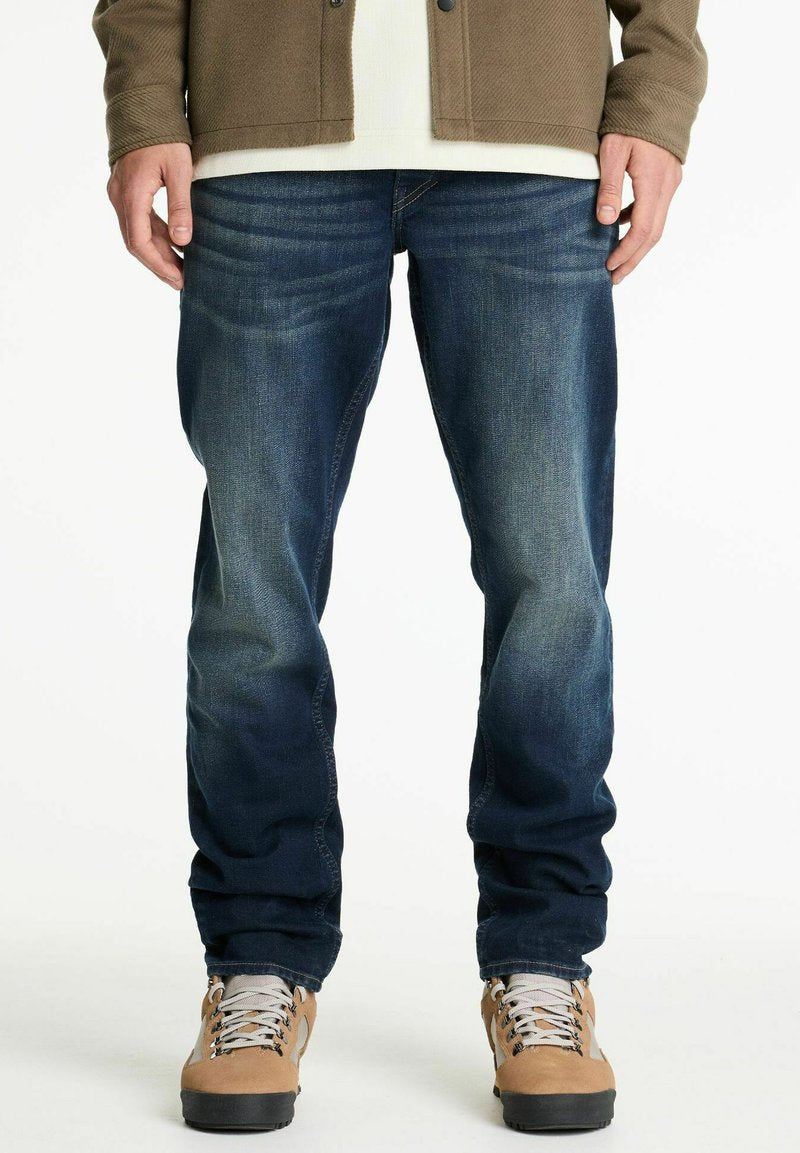 Blaue Denim-Jeans mit einer lockeren Passform und dezentem Verblassen, kombiniert mit beigen Wanderstiefeln mit grauen Schnürsenkeln und einer strukturierten Außensohle.