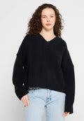 Schwarzer V-Ausschnitt-Pullover mit lockerer Passform, gerippten Bündchen und Saum, aus weichem Material, kombiniert mit hellblauen Jeans.