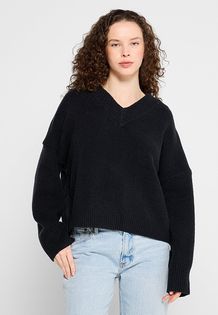 Schwarzer V-Ausschnitt-Pullover mit lockerer Passform, gerippten Bündchen und Saum, aus weichem Material, kombiniert mit hellblauen Jeans.