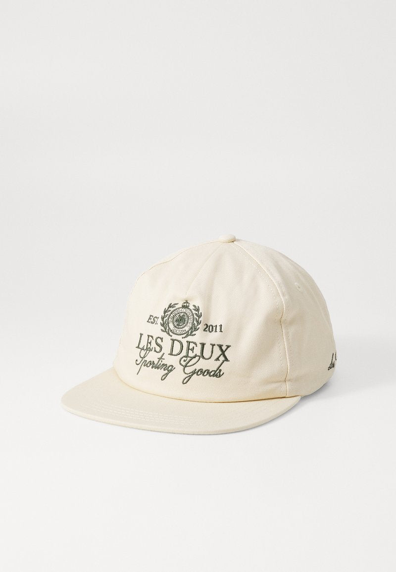 Beige Kappe mit gebogenem Schirm, die grün gestickte Texte und Designs aufweist, einschließlich "LES DEUX Sporting Goods" und Lorbeer-Grafiken.