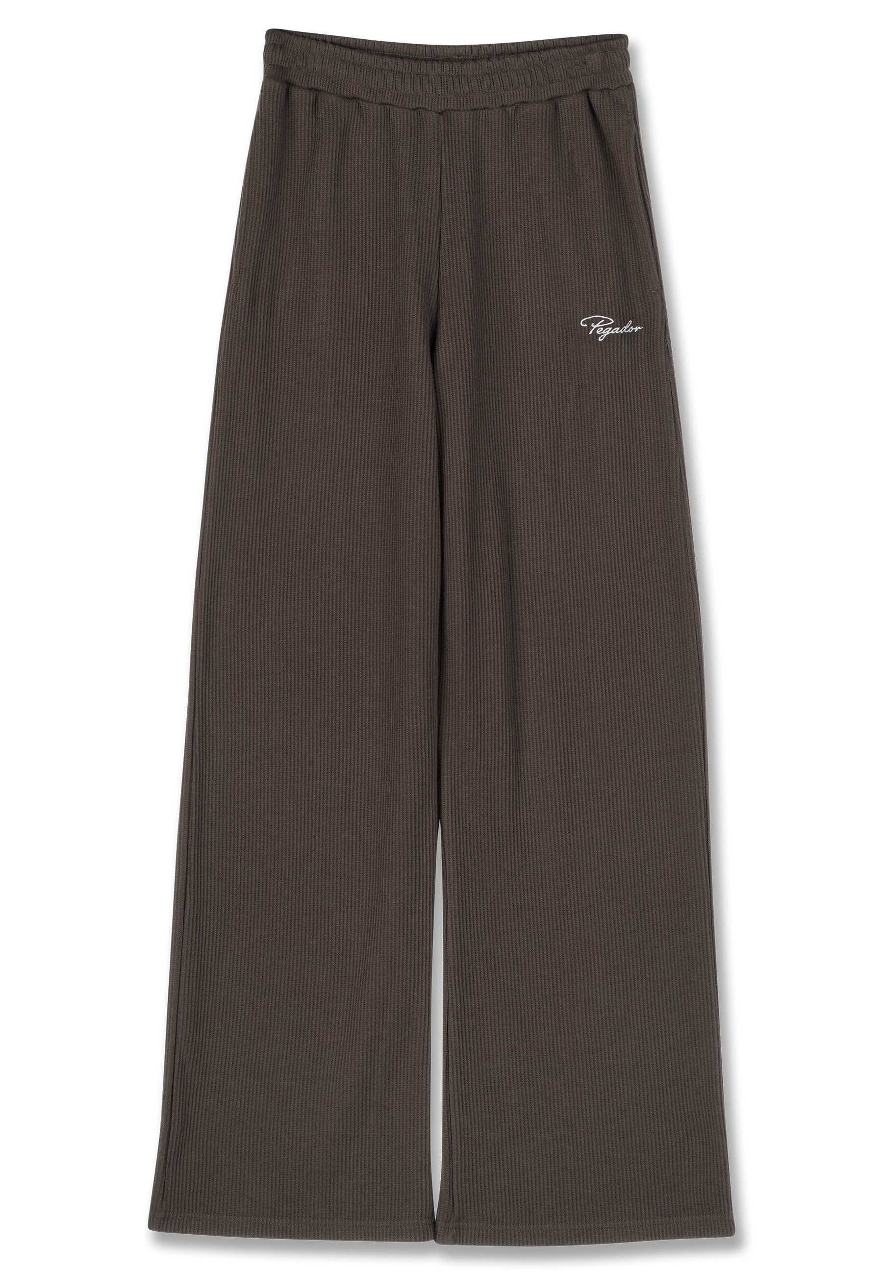 Braune, weit geschnittene Hose mit geripptem Stoff und elastischem Bund. Verfügt über den weißen, auf der linken Hüfte eingestickten Markennamen.