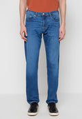 Blaue Jeans aus Denim mit geradem Bein, fünf Taschen und dezenter Naht. Kombiniert mit schwarzen Turnschuhen und einem rostfarbenen Hemd.