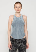 Frau mit hellen Haaren in einem ärmellosen, hochgeschlossenem, vertikal gestreiften blau-weißen Oberteil und schwarzen Acid-Wash-Jeans vor einem schlichten grauen Hintergrund.