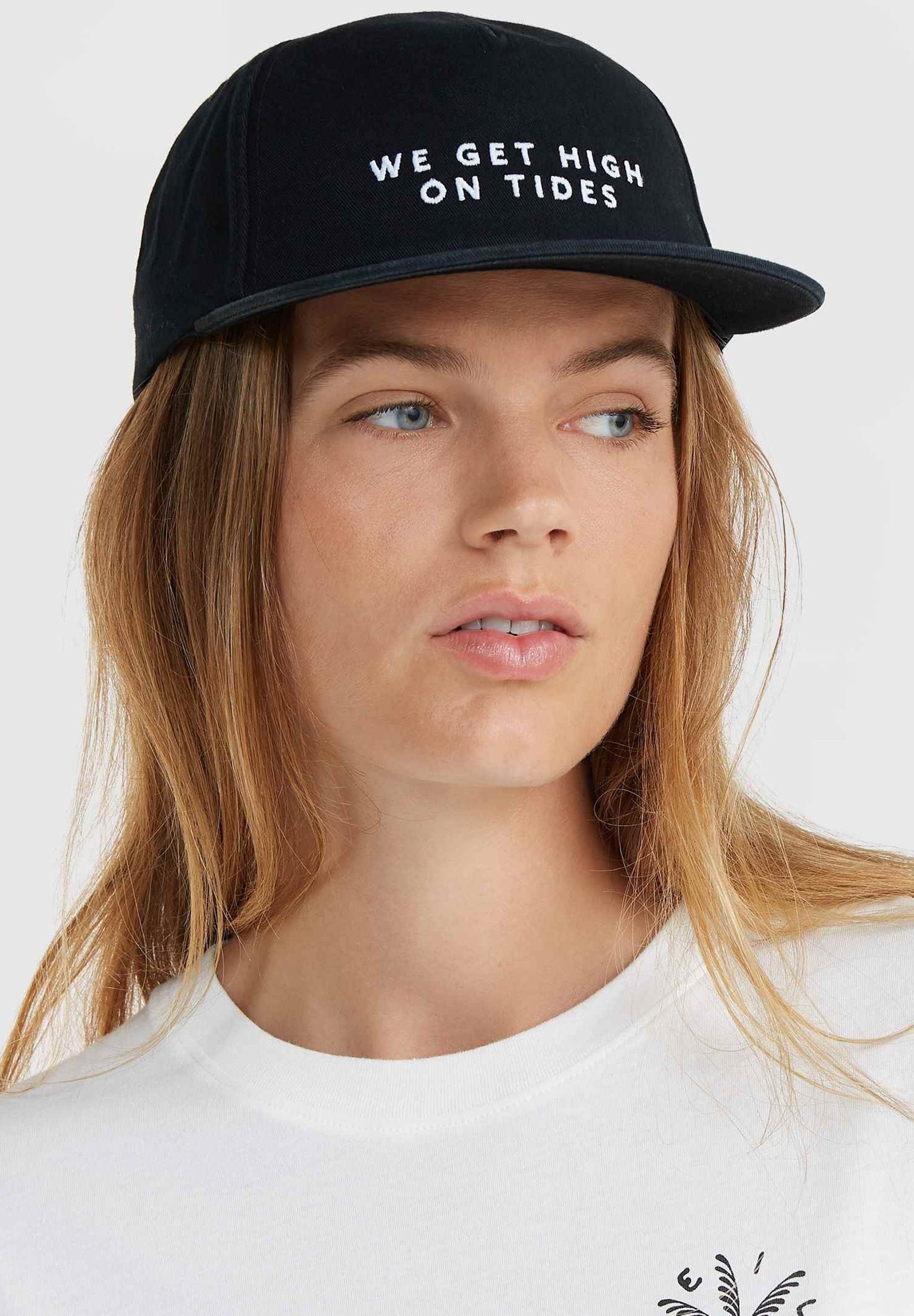 Schwarze Mütze mit flachem Schirm und gesticktem weißen Text "WIR WERDEN HIGH AUF GELOSTEN." Tragen mit einem weißen Rundhals-T-Shirt. Glatte Stoffstruktur.