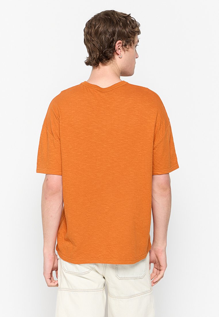 Orange Baumwoll-T-Shirt mit lockerem Schnitt, kurzen Ärmeln und V-Ausschnitt. Der Stoff hat ein strukturierter Aussehen mit subtilen Variationen.