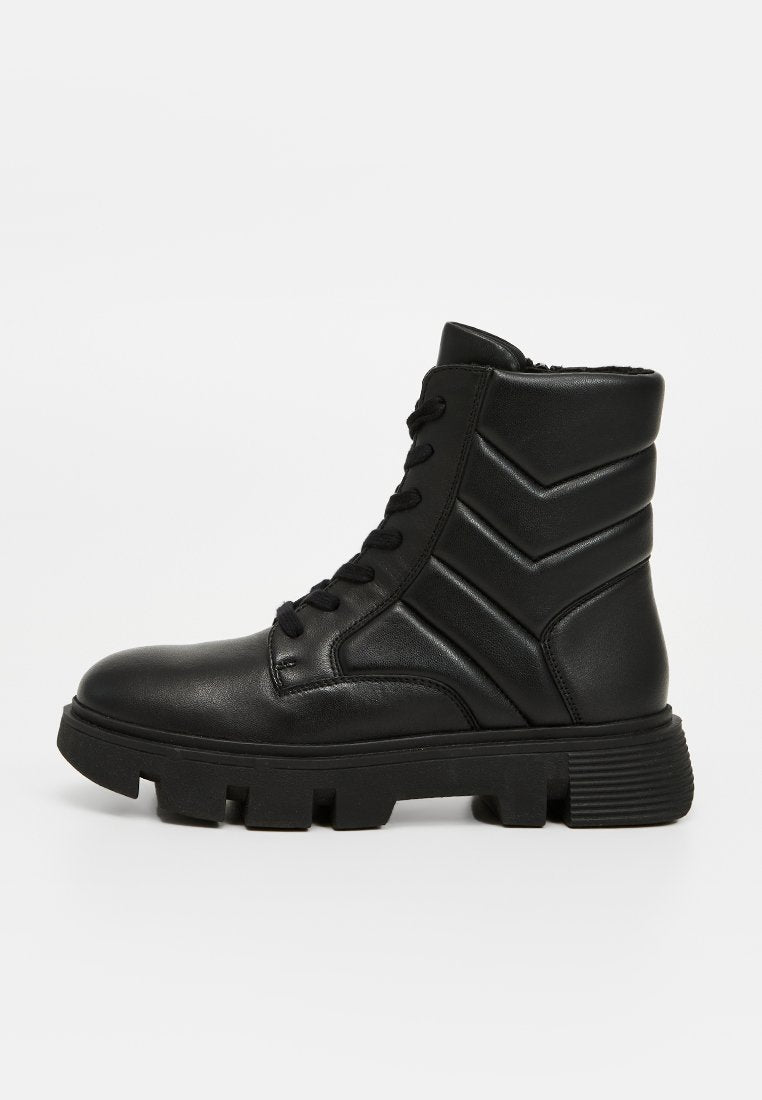 Schwarze Knöchelboots aus glattem Leder mit strukturiertem, dicker Zickzack-Textur am Schaft, Schnürverschluss und einer klobigen, gerillten Sohle.