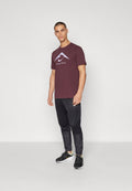 Bordeauxrotes T-Shirt mit kurzen Ärmeln und Logo, kombiniert mit schwarzen, zulaufenden Hosen und schwarzen Turnschuhen. Einfaches Design mit glatter Textur.