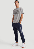 Graues T-Shirt mit schwarzem "O'NEILL"-Logo, kombiniert mit marineblauen Jogginghosen, die weißen "O'NEILL"-Text tragen. Weiße Sportschuhe runden das Outfit ab.