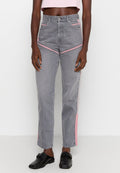 Person, der hochgeschnittene graue Jeans mit rosa Streifen an den Seiten und vorne trägt, kombiniert mit schwarzen Slippern und einem hellrosa Cropped-Top.