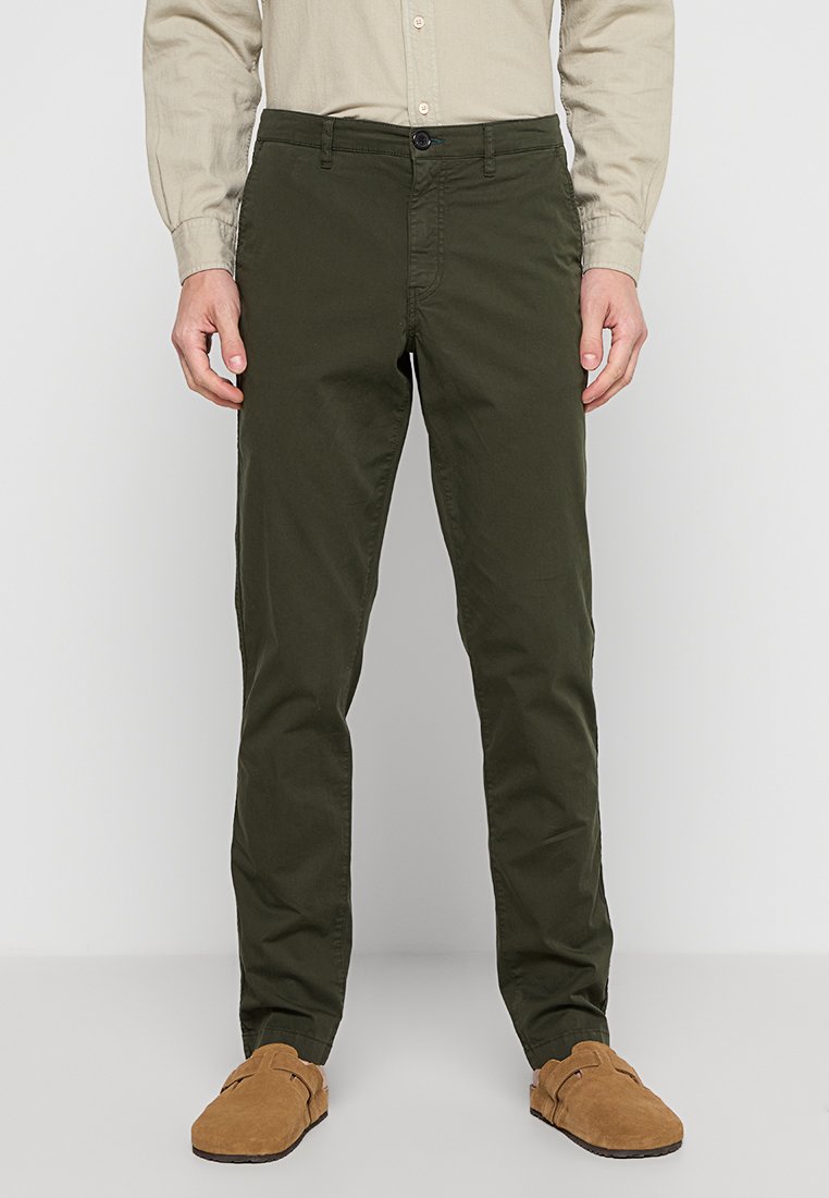 Olivgrüne Chinos mit geradem Schnitt, aus einem Baumwollgemisch, mit Knopfverschluss und Gürtelschlaufen, kombiniert mit braunen Wildleder-Schlupfschuhen.