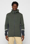 Mann mit einer grünen Zip-Up-Hoodie mit dunkelgrauen Ärmeln und CMP-Logos, kombiniert mit beigen Cargo-Hosen, steht vor einem einfarbigen Hintergrund.