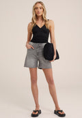 Schwarzes, figurbetontes Tanktop, graue Jeansshorts und schwarze Plateausandalen. Das Model hält eine schwarze, gesteppte Tasche. Schlichtes, modernes Outfit-Design.