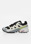 Schwarzer, grauer und weißer Salomon Trailrunning-Schuh mit gelbem Logo, gelben Akzenten und robuster schwarzer Außensohle für Grip auf unebenem Gelände.