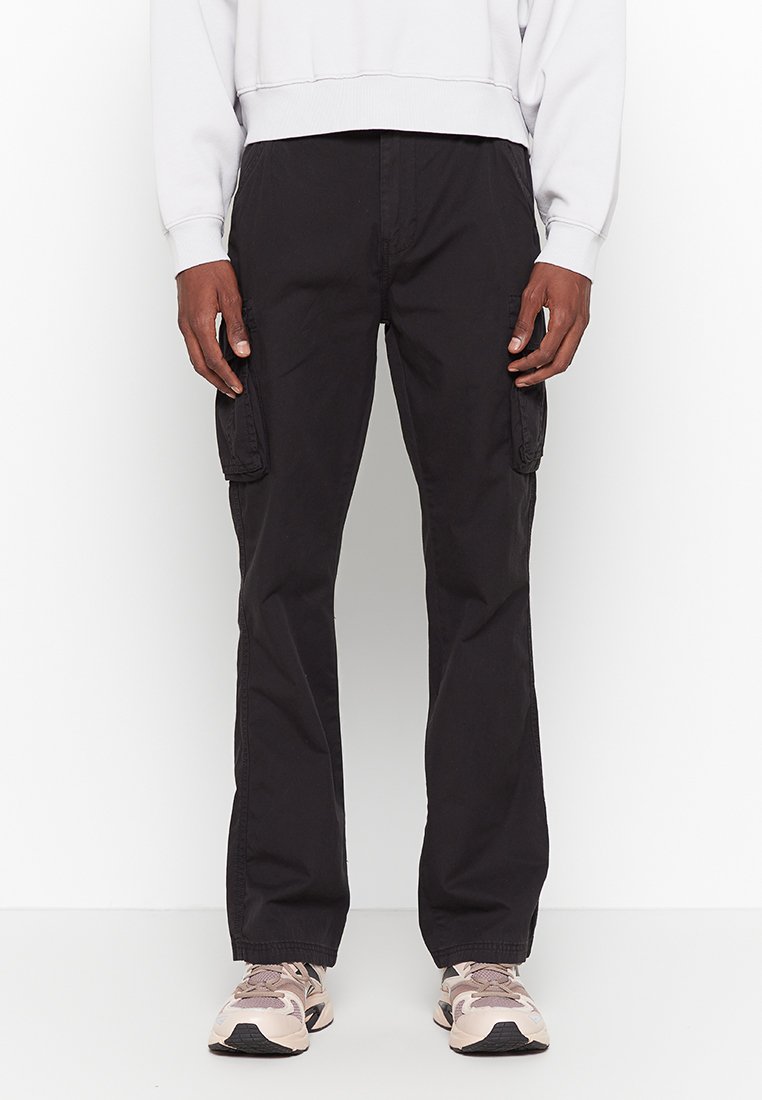 Schwarze Cargo-Hosen mit Seitentaschen, aus robustem Material gefertigt. Figurbetontes Design mit geradem Bein. Kombiniert mit einem leichten Sweatshirt und Sneakers.