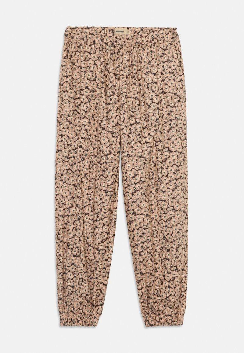 Blumenmuster-Hose mit elastischem Bund und Knöchellöchern. Der Stoff hat einen beigen Hintergrund mit rosa und grünen Blumen.