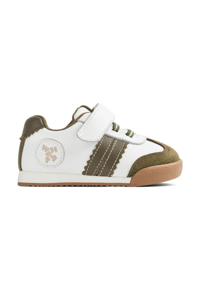Weißer Sneaker mit grünen Akzenten, Wildleder an Zehen- und Fersenbereich, Schnürsenkel mit Klettverschluss und einem gemusterten Design an den Seiten mit einem runden Logo.