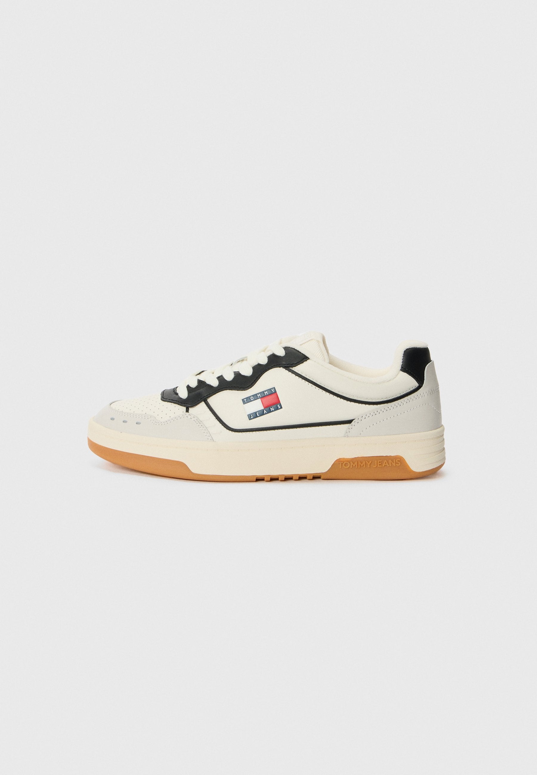 Weiße und schwarze Sneaker mit perforierter Zehenpartie, Gummisohle und einem Logopatch mit rot-blauen und weißen Streifen an der Seite.