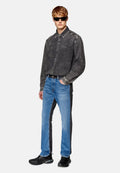 Graues Denim-Hemd mit Kragen, kombiniert mit blauen Jeans, die seitliche schwarze Einsätze haben. Das Modell trägt schwarze Sneakers und Sonnenbrille.