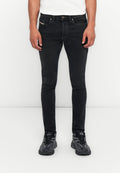 Mann in eng anliegenden schwarzen Jeans, weißem Hemd und schwarzen Diesel-Sneakern, der vor einem schlichten weißen Hintergrund steht.