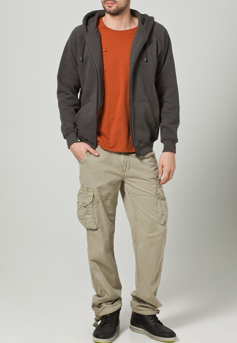 Dunkelgraue Zip-Hoodie über einem orangefarbenen T-Shirt, kombiniert mit beigen Cargo-Shorts. Verfügt über Taschen und einen lässigen Schnitt mit Sneakers.