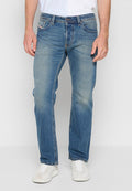 Mann in verblassten blauen Jeans und weißen Sneakers, der vor einem schlichten weißen Hintergrund steht.