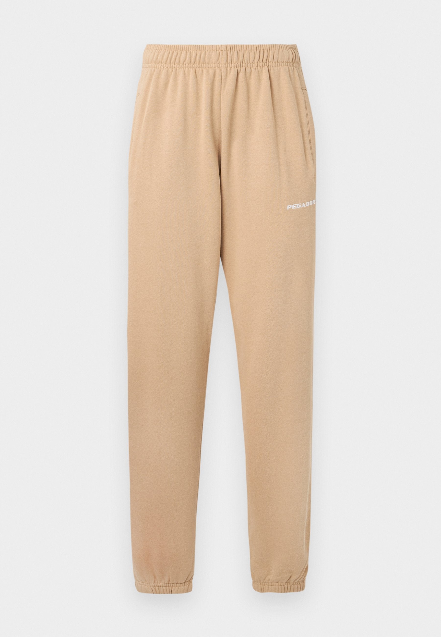 Beige Jogginghose mit elastischem Bund, schmal zulaufenden Beinen und seitlichen Taschen. Auf dem linken Oberschenkel befindet sich der kleine weiße Schriftzug "PEGADOR".
