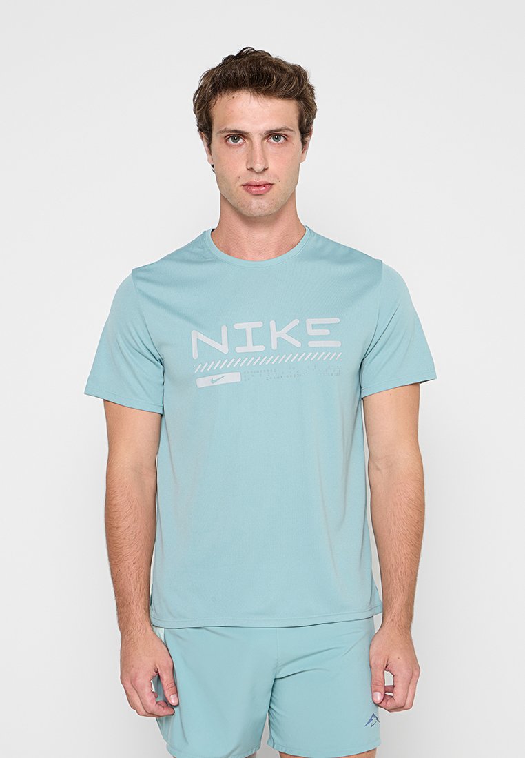 Junger Mann, der ein hellblaues Nike-T-Shirt und passende Shorts trägt, vor einem schlichten hellen Hintergrund stehend, schaut nach vorne.