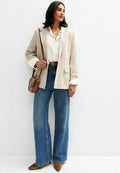 Beige gestreifter Blazer, weißes Hemd, brauer Gürtel, weite blaue Jeans und braune High Heels. Umhängetasche mit goldener Verschlussdetail.