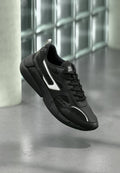 Schwarzer Sportschuh mit mesh-Obermaterial, glatten Lederakzenten und einer Gummisohle mit strukturierten Details. Weißes Logodesign auf der Zunge.