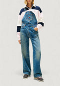 Jeans-Latzhose in Hellblau mit weitem Bein, Fronttasche und verstellbaren Trägern. Kombiniert mit einem Sweatshirt im Color-Block-Design.