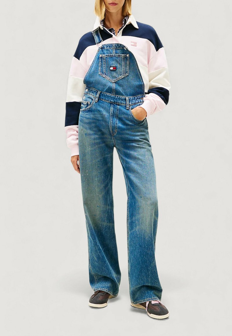 Jeans-Latzhose in Hellblau mit weitem Bein, Fronttasche und verstellbaren Trägern. Kombiniert mit einem Sweatshirt im Color-Block-Design.