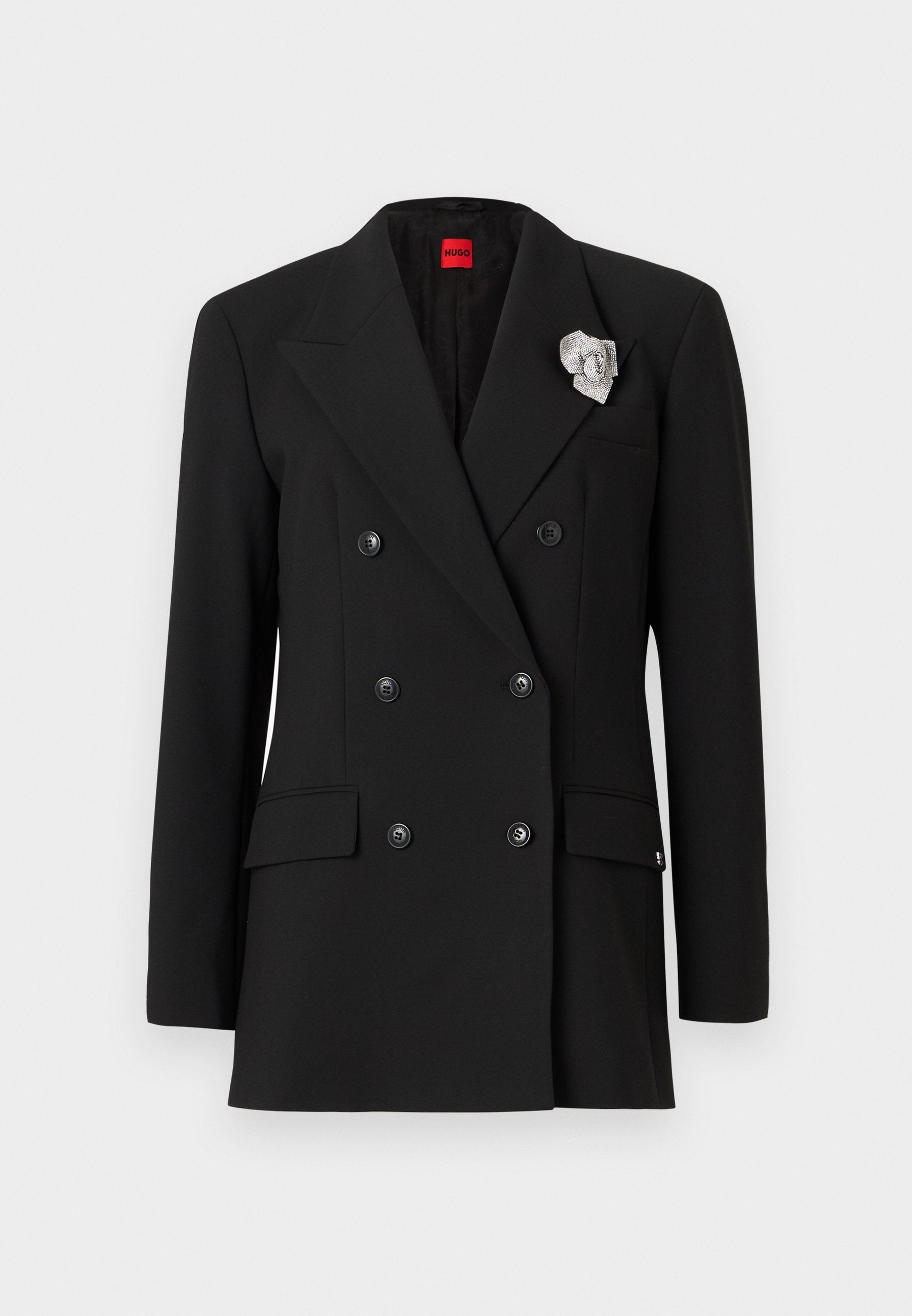 Schwarzer doppelreihiger Blazer mit großen Revers, zwei Fronttaschen und einem silbernen Broschenakzent am Revers. Glatte Stofftextur.