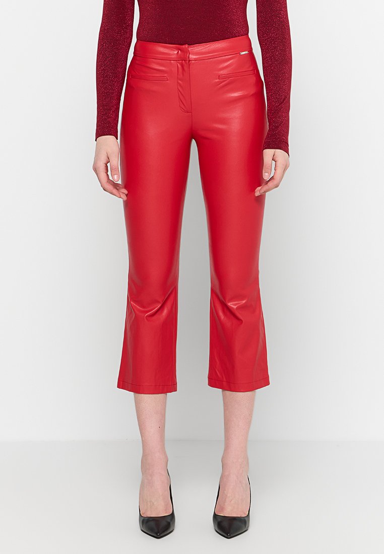Rote Kunstleder-Cropped-Hosen mit tailliertem Design, Fronttaschen und einer glatten, glänzenden Textur. Kombiniert mit schwarzen High Heels.