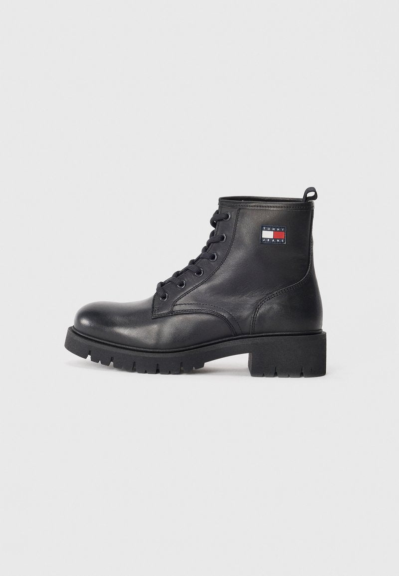 Schwarze Leder-Stiefel bis zum Knöchel mit runder Zehenpartie, Schnürverschluss auf der Vorderseite, robuster Gummisohle und einem Logopatch an der Seite. Glatte Textur, stabile Konstruktion.