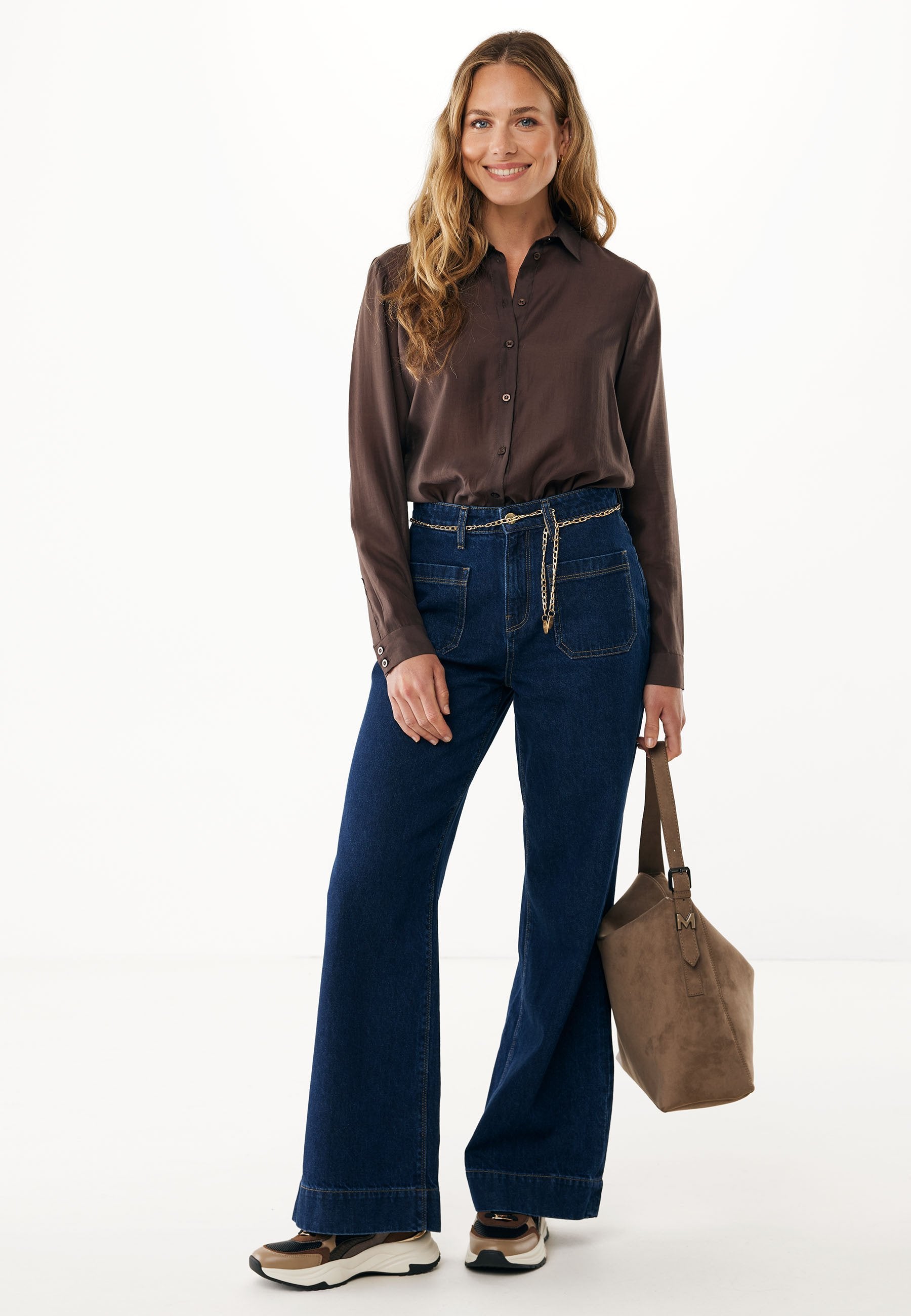 Dunkelbraune Button-Up-Bluse, hoch geschnittene blaue Denim-Wide-Leg-Hosen und beiger Wildlederhandtasche mit Kettenakzent. Sneaker mit einem schwarzen und beigen Design.